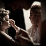 A professional makeup artist works on a bride's look in soft lighting before a photoshoot.
