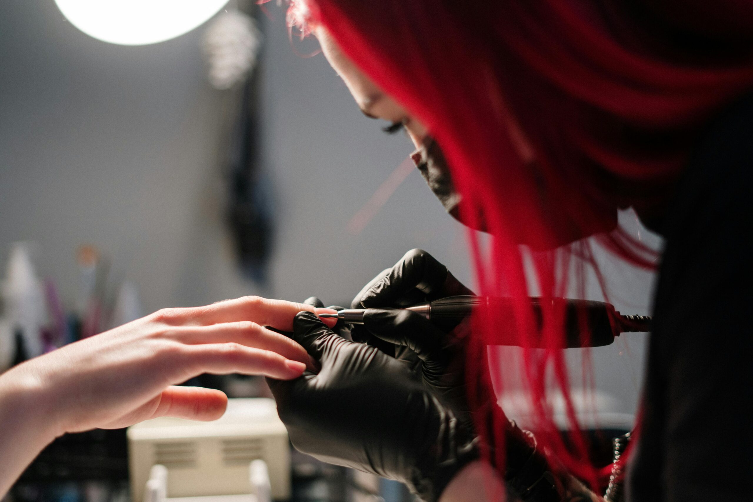A nail technician with red hair performs a manicure wearing black gloves in a salon.