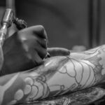 Artistic black and white photo capturing the detailed process of tattooing an arm.